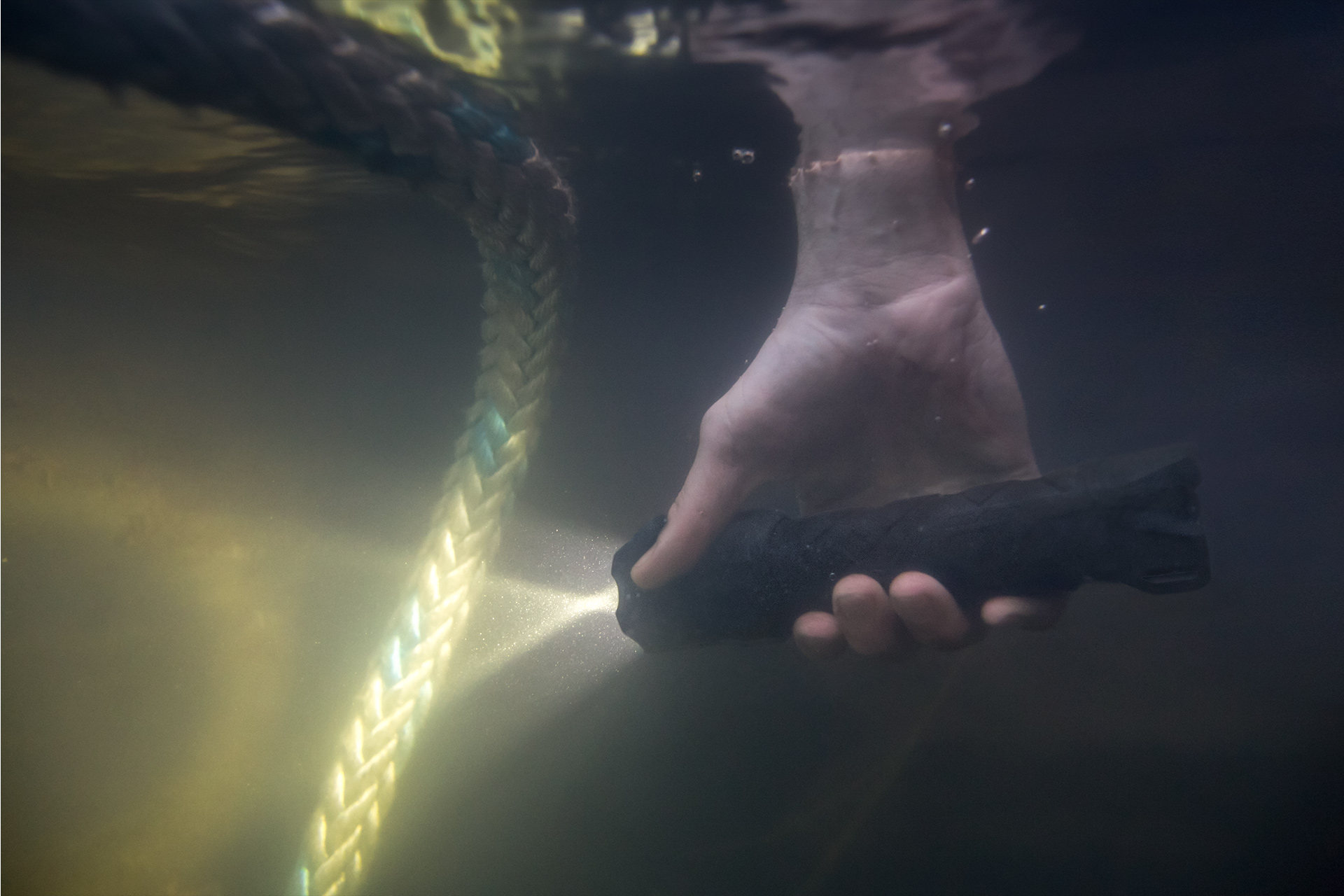 Brand Photography for Coast Products showing hand holding waterproof flashlight under water with light shining on rope