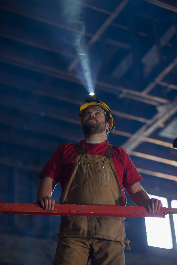 Construction worker on lift in warehouse wearing a Coast Headlamp on helmet with beam shining towards ceiling