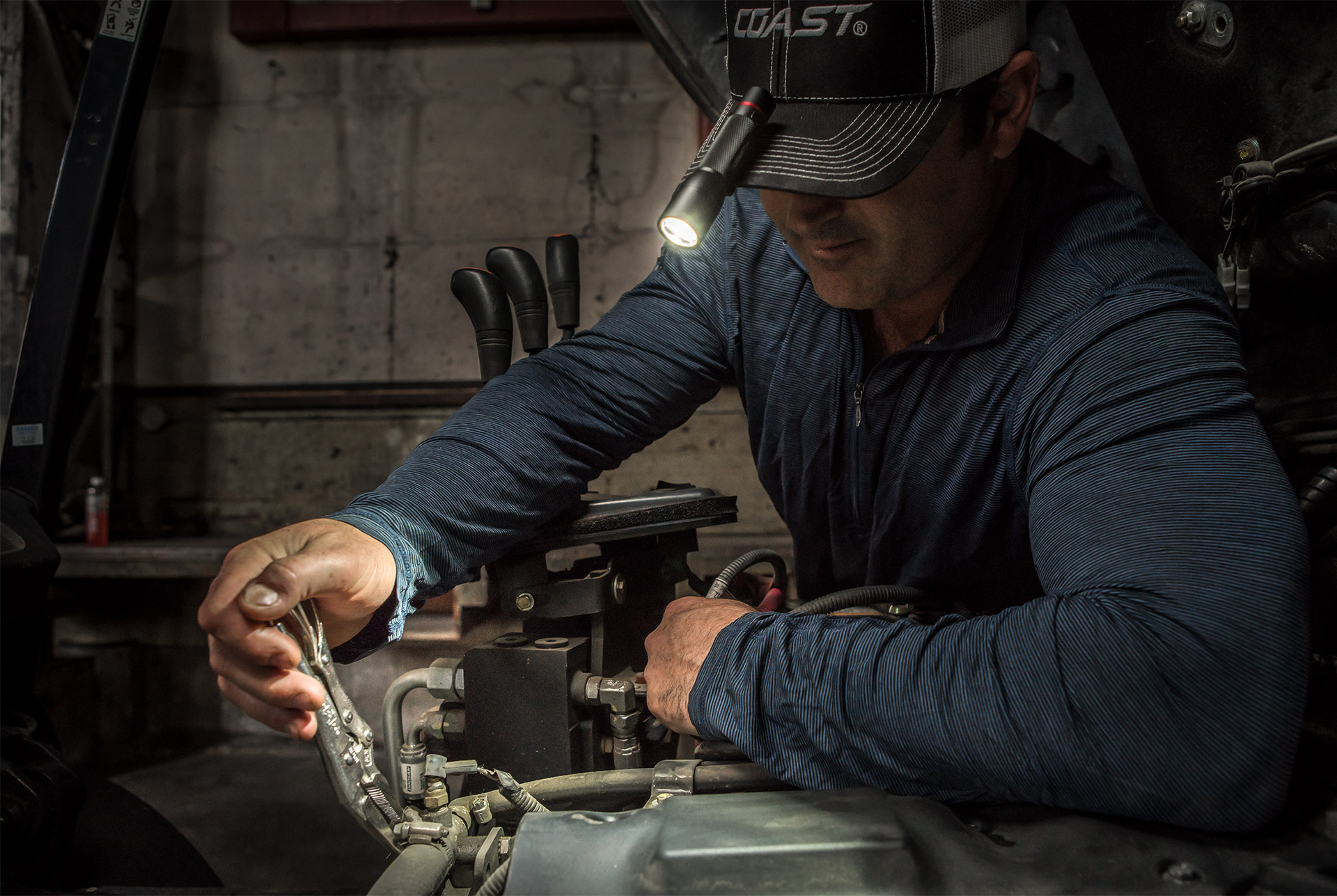 Man working on machinery with Coast Products flashlight on cap